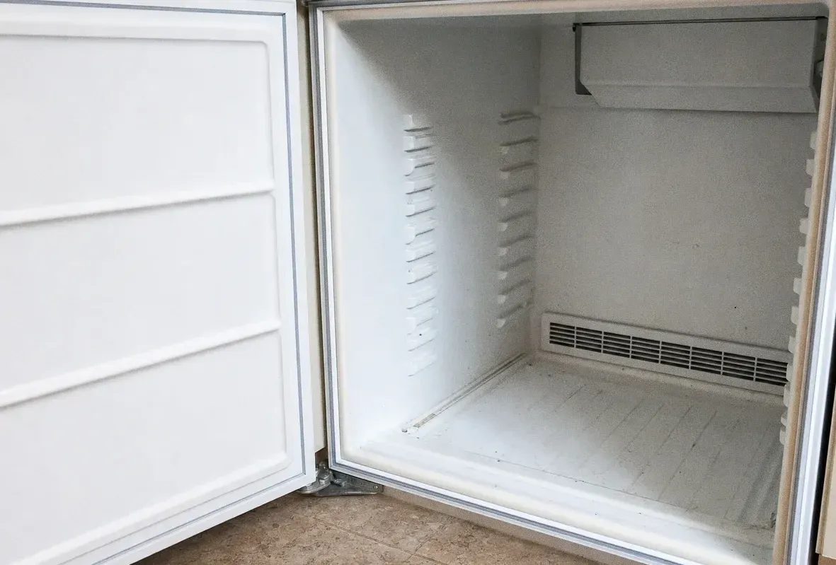Empty upright refrigerator compartment with the door swung wide, bare shelf rails and a vent grille low on the back wall